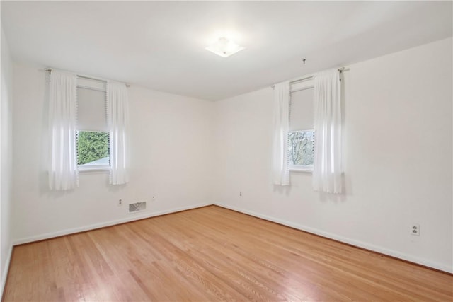 spare room featuring light wood finished floors, visible vents, and baseboards