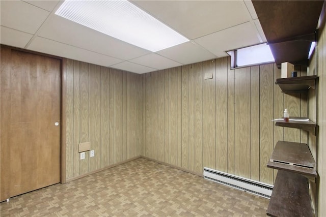 below grade area featuring a baseboard heating unit, a drop ceiling, and wood walls