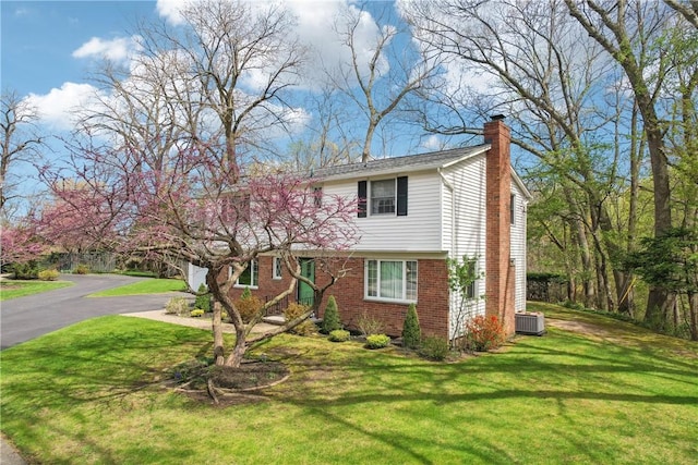 colonial house with central AC unit, brick siding, a chimney, and a front yard