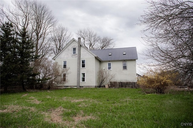back of house with a chimney, metal roof, and a yard