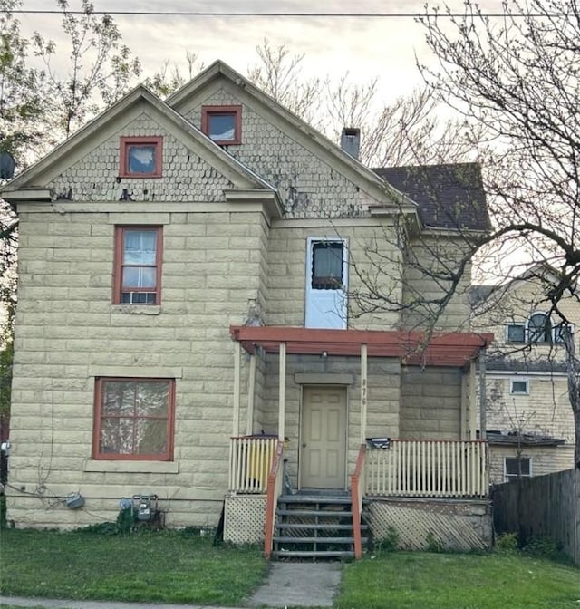 victorian home with covered porch, fence, stone siding, and a front yard