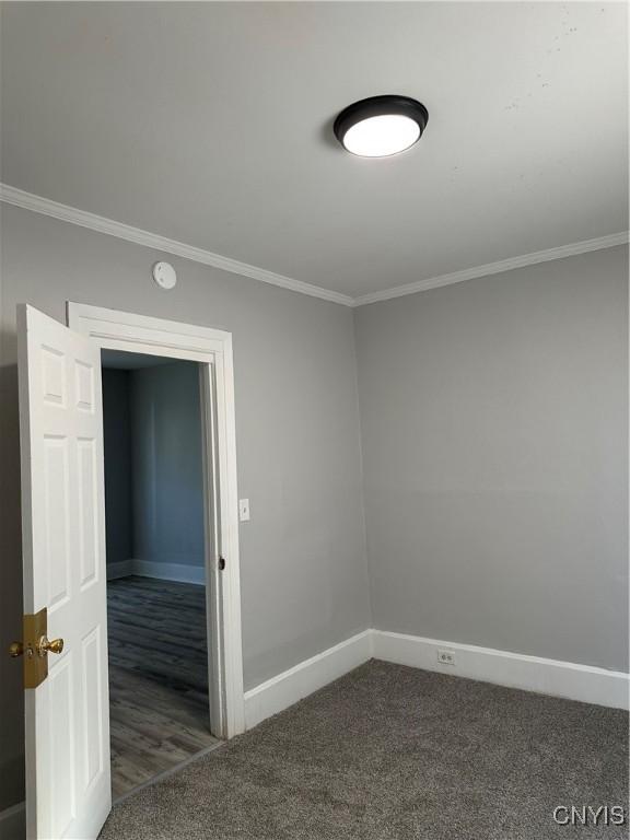 carpeted empty room featuring crown molding and baseboards