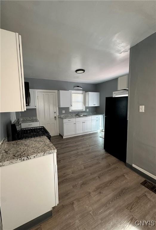 kitchen featuring baseboards, light stone counters, white cabinetry, dark wood-type flooring, and black appliances