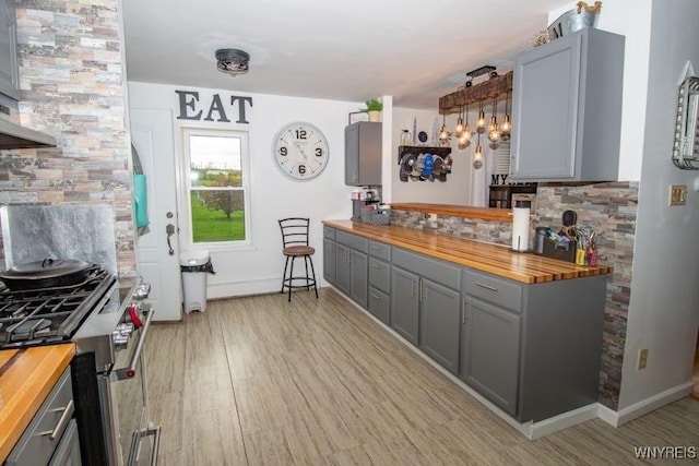 kitchen with gray cabinets, high end stainless steel range oven, tasteful backsplash, and butcher block countertops