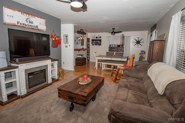 living area with a stone fireplace, wood finished floors, and ceiling fan