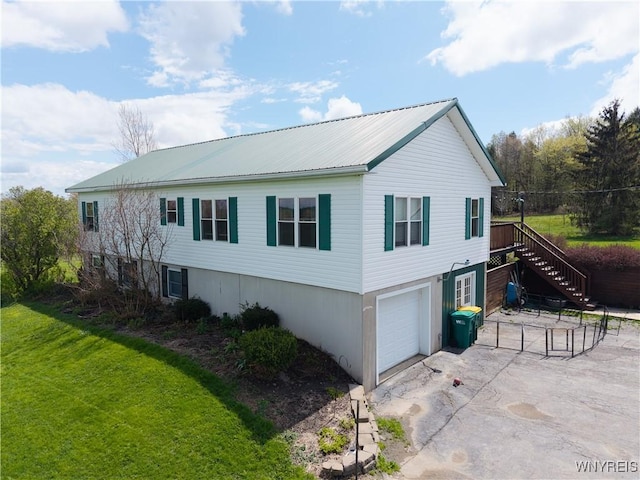 view of property exterior with stairway, asphalt driveway, a garage, a yard, and metal roof
