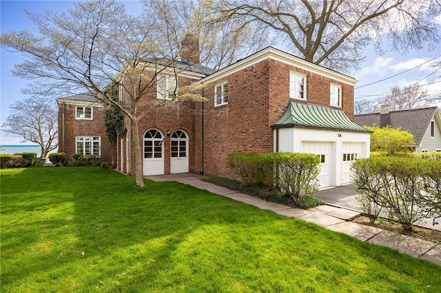 rear view of property featuring a chimney, brick siding, a lawn, and an attached garage