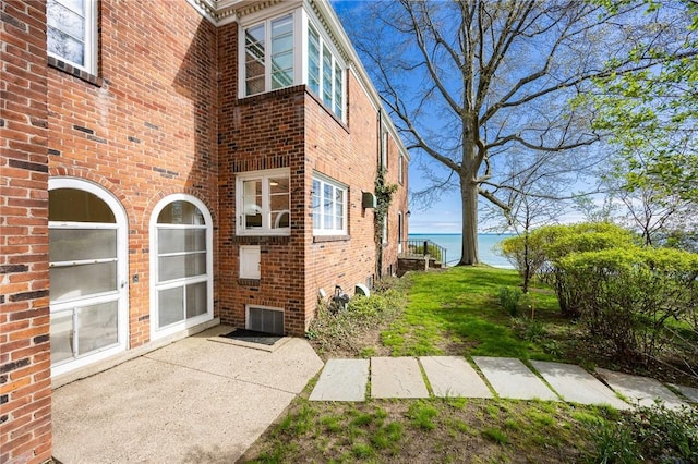 back of property featuring a water view, brick siding, and a patio