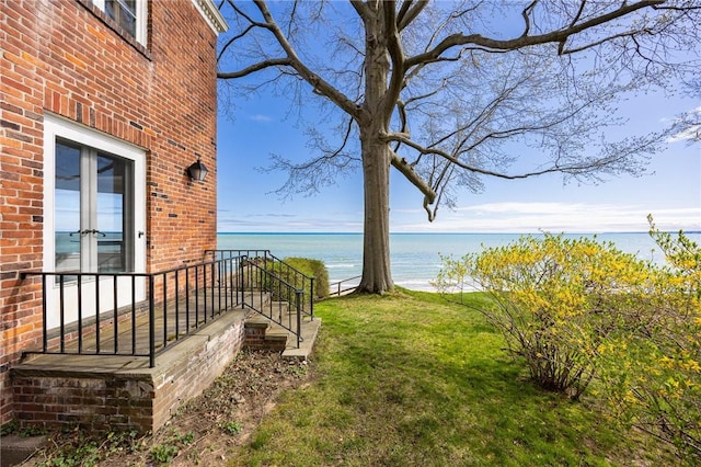 view of green lawn with french doors and a water view