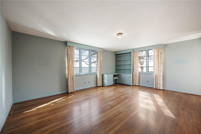 empty room featuring wood finished floors, baseboards, and built in features