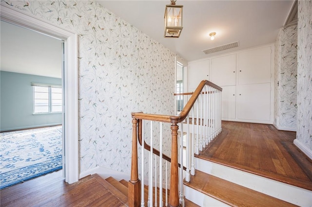 stairs with wallpapered walls, wood finished floors, and baseboards