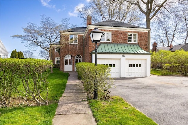 view of front of property featuring a chimney, a garage, brick siding, a standing seam roof, and driveway