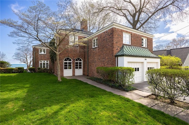 view of front facade featuring brick siding, an attached garage, a front yard, a chimney, and a standing seam roof