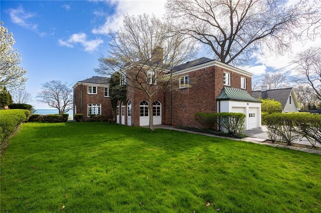 back of property with brick siding, concrete driveway, a chimney, a garage, and a yard