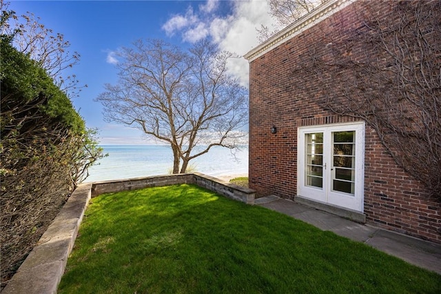 view of grassy yard with a water view and french doors