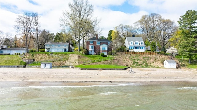 view of front of house featuring view of water and beach, a storage shed, and an outbuilding