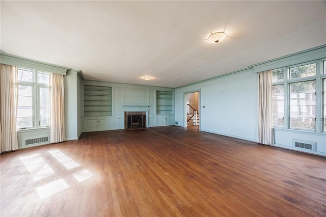unfurnished living room with built in shelves, dark wood finished floors, baseboards, a brick fireplace, and crown molding