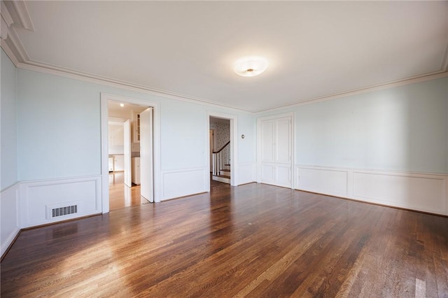 unfurnished room featuring wood finished floors, a decorative wall, ornamental molding, stairs, and a wainscoted wall