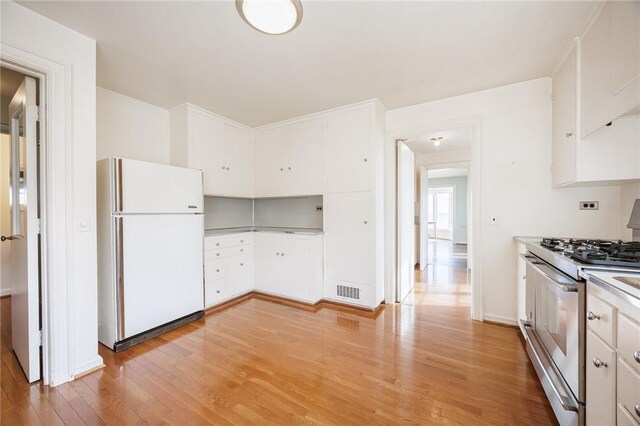 kitchen with freestanding refrigerator, stainless steel gas range, light wood-style floors, white cabinets, and light countertops