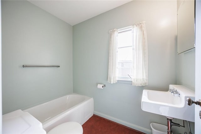 bathroom featuring a tub to relax in, baseboards, toilet, and a sink