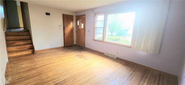 empty room featuring light wood-type flooring, stairs, and baseboards