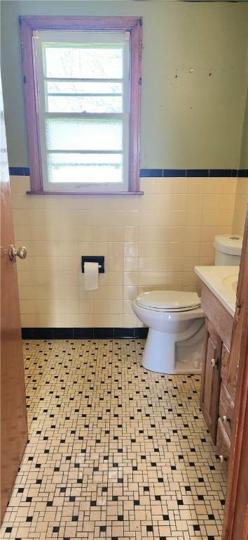bathroom with tile walls, toilet, healthy amount of natural light, wainscoting, and vanity