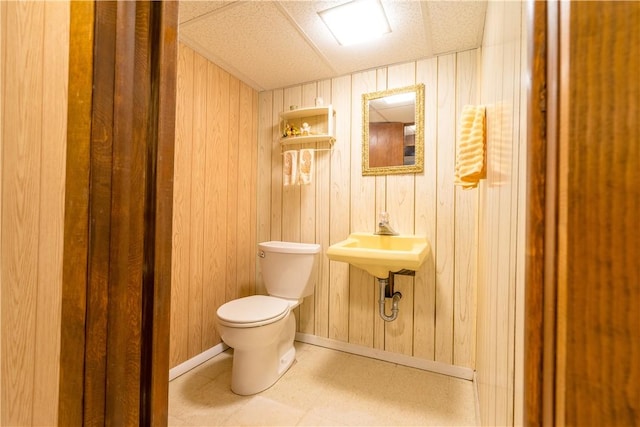 half bathroom featuring toilet, tile patterned floors, wood walls, baseboards, and a sink