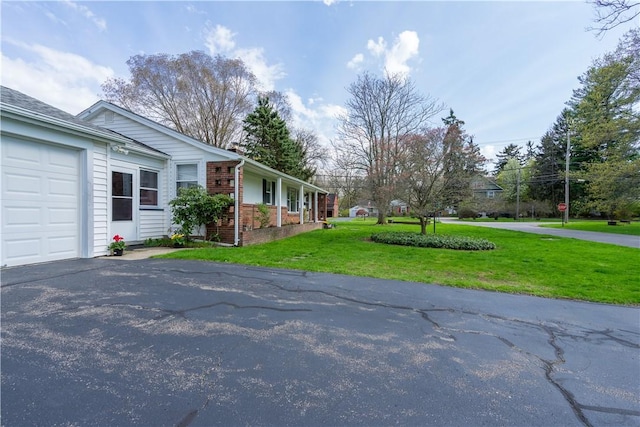 view of property exterior with asphalt driveway, a lawn, a garage, and brick siding