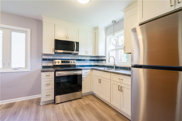 kitchen featuring appliances with stainless steel finishes, a sink, dark countertops, light wood-style floors, and tasteful backsplash