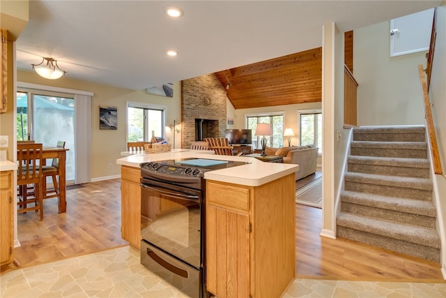 kitchen featuring black electric range oven, light countertops, recessed lighting, a brick fireplace, and light wood finished floors