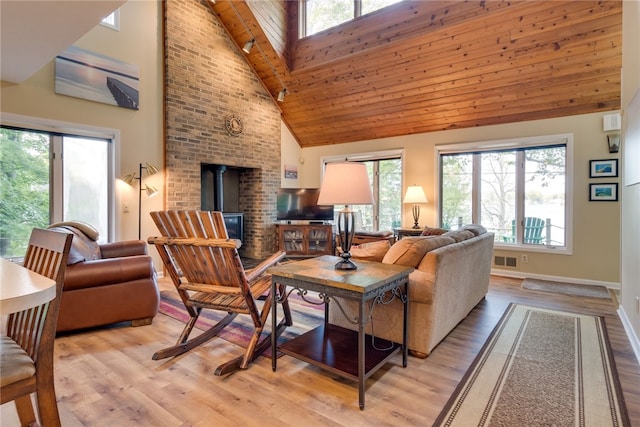 living room with high vaulted ceiling, a wood stove, plenty of natural light, light wood finished floors, and baseboards