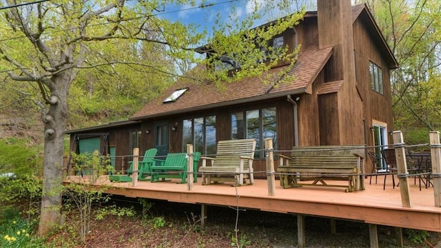 rear view of property featuring roof with shingles, a deck, and a chimney