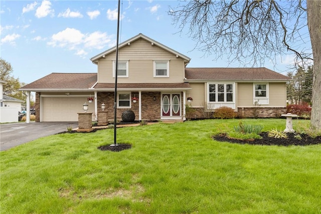split level home with asphalt driveway, a garage, a front yard, and brick siding