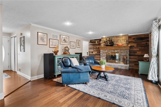 living area featuring a textured ceiling, baseboards, wood finished floors, a stone fireplace, and ornamental molding