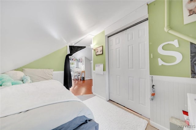 bedroom featuring vaulted ceiling, wainscoting, and a closet