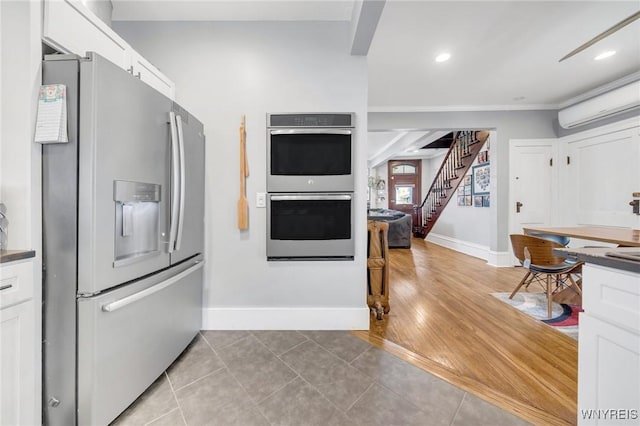 kitchen with appliances with stainless steel finishes, a wall mounted air conditioner, baseboards, white cabinetry, and dark countertops