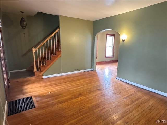 1270 W Belden Ave, Syracuse, NY 13204 - unfurnished living room featuring arched walkways, hardwood / wood-style flooring, baseboards, and stairway