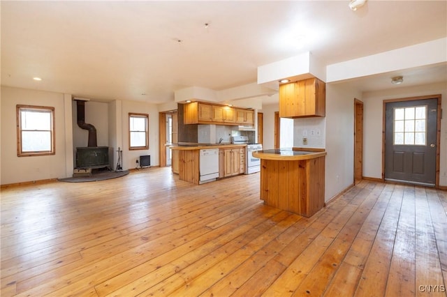 kitchen featuring white appliances, open floor plan, a peninsula, light wood-style floors, and a wood stove