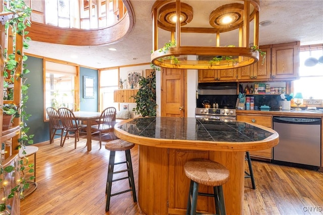 kitchen featuring dishwasher, brown cabinetry, light wood-type flooring, and a kitchen breakfast bar
