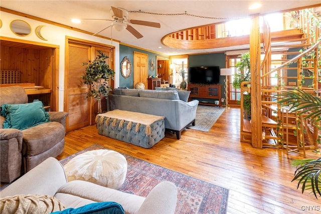 living area with hardwood / wood-style flooring, ceiling fan, crown molding, and stairway