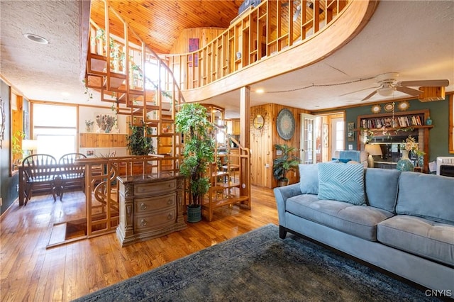 living area featuring wood finished floors, a ceiling fan, stairs, and wood walls