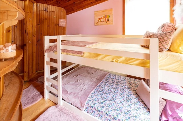 bedroom with lofted ceiling, wooden ceiling, wood finished floors, and wood walls