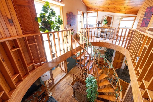 staircase with healthy amount of natural light, wood finished floors, wood ceiling, lofted ceiling, and arched walkways