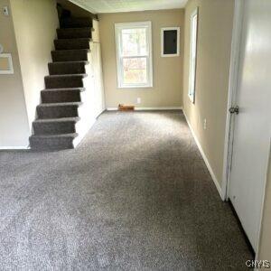 unfurnished living room featuring stairs, healthy amount of natural light, carpet flooring, and baseboards