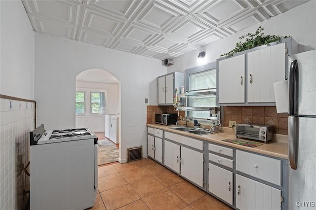 kitchen with appliances with stainless steel finishes, a sink, arched walkways, light countertops, and decorative backsplash