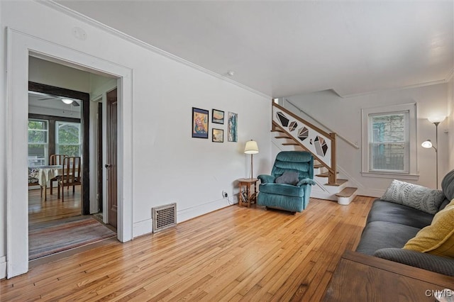 living room featuring stairs, hardwood / wood-style flooring, ornamental molding, and baseboards