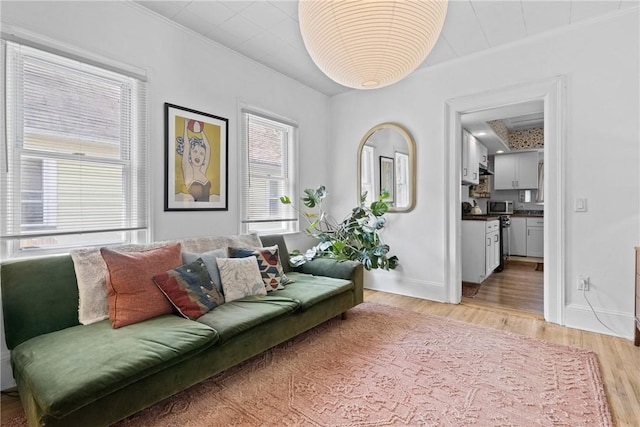 living area featuring light wood-style flooring, crown molding, and baseboards