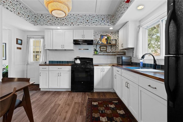 kitchen with black appliances, under cabinet range hood, wood counters, wood finished floors, and white cabinets