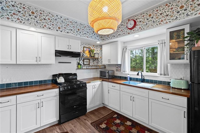 kitchen featuring butcher block counters, black appliances, a sink, under cabinet range hood, and white cabinets