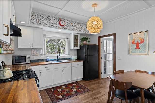 kitchen featuring wooden counters, a sink, black appliances, tasteful backsplash, and wood finished floors
